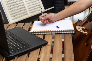 Detail of a young man taking notes in a notebook with a computer on a portable wooden table with...