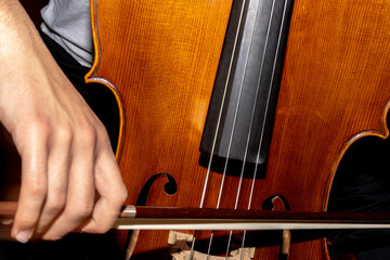 detail of a man playing the wooden cello rubbing the strings with the bow to get classical music © Avelino