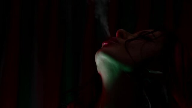 prostitute is smoking in nightclub or bordello, closeup portrait of woman in darkness