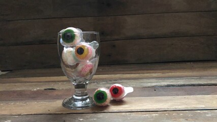 Decorative funny halloween treat,wine glass has colorful jelly eyeballs on old wood...