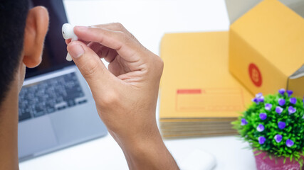 A person's hand with white wireless headphones Online talk In front there are notebooks, parcel boxes, online sales concept, covid-19, at home, looking for work at leisure.