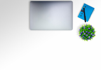 White desk There is a vignette shadow in the top right corner. On the table, there is a notebook, a pen, a small tree, taken from the top corner with a copy space concept on the desk.