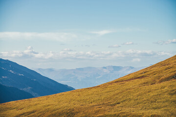 Minimalist autumn landscape with diagonal of sunlit orange mountainside on background of mountains silhouettes on horizon. Minimal mountain scenery with slope of hill in golden sunlight in autumn time