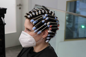 young woman, girl is getting perm,  hair curlers on head at hairdressers salon, wearing mask because of corona virus - obrazy, fototapety, plakaty