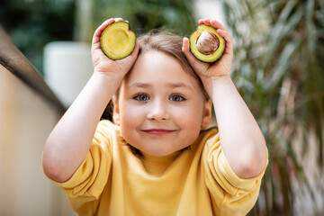 Little girl in yellow sweatshirt holding cut avocado, healthy eating concept