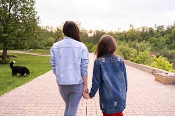 Mother and teenage daughter walking in a park, holding hands, happy young caucasian woman with long hair and teenage girl hanging out in a city, lifestyle family