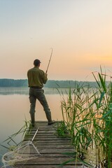 Angler catching the fish at dawn from wooden pier
