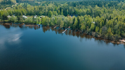 A beautiful scenery, a lake, a forest, a small village from a bird's eye view. Ideal for fishing, pontoon bridge. The clouds are reflected in deep water. Aerial photography, view from a drone.