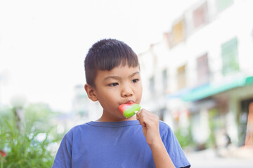 Portrait image of 6-7 years old kid. Happy Asian child boy eating and biting a red ice cream. Summer season, Delicious feeling, childhood sloppy face.
