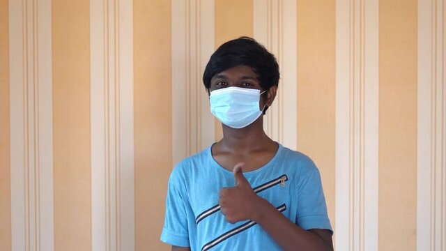 Portrait of an Indian teen giving thumbs up to the camera while wearing face mask