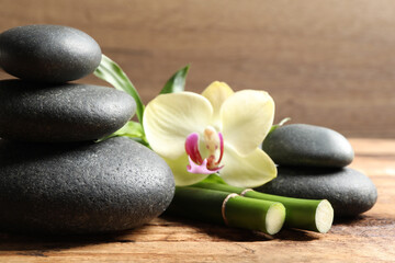 Fototapeta na wymiar Spa stones, bamboo stems and beautiful orchid flower on wooden table, closeup