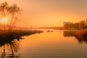 Naklejka na ściany i meble Foggy sunset over the lake near the city