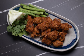 Fried Pork Larb (larb tord) in a long plate on a black background. Spicy Thai food of Isan region.