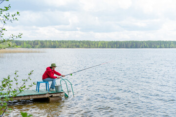 A fisherman with a hat with a fishing rod sits on the bank of the river.