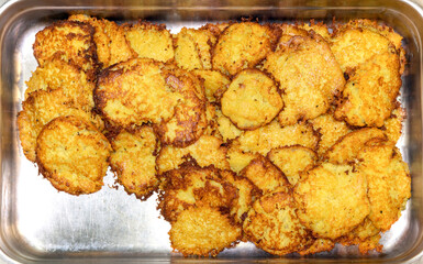 Lots of fried potato pancakes in a metal dish.