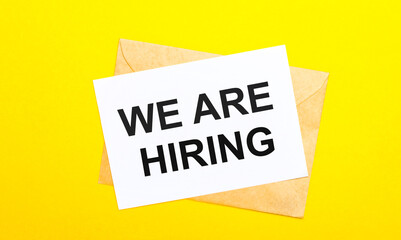 On a yellow background, an envelope and a card with the text WE ARE HIRING. View from above