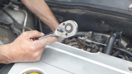 Mechanic repairing car with ratchet wrench.