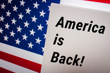 Conceptual keyword America is Back! on card on US flag from a little bit diagonal angle. Business, economy, social concept of America. American patriotic message concept on national flag