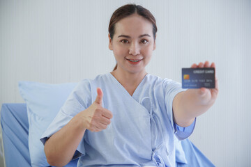 Portrait of Asian young patient woman holding blue credit card in her hand, smile and thumb up in...