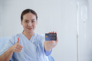 Selective focus on blue credit card that Asian young patient woman holding in hand, smile and thumb...