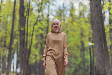 Islamic beautiful woman in a Muslim dress standing on a summer park street background forest autumn...