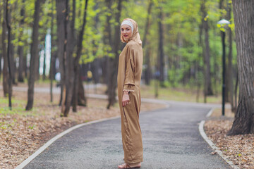 Islamic beautiful woman in a Muslim dress standing on a summer park street background forest autumn...