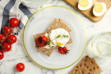 Fresh rye crispbreads with poached egg, cream cheese and grilled tomatoes on white marble table, flat lay