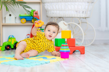 baby boy plays in the children's room in a yellow bodysuit with bright colorful toys