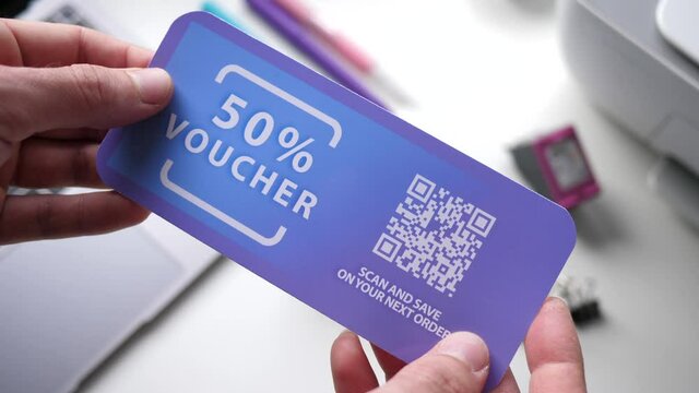 Hands holding a 50% off voucher coupon with a QR code on the side to be scanned.