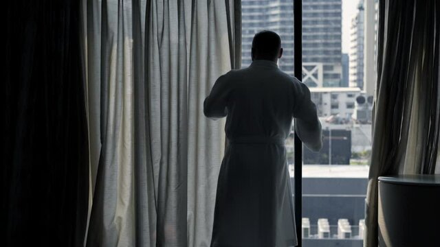 Man in bathrobe unveil curtains and admire view from window at home