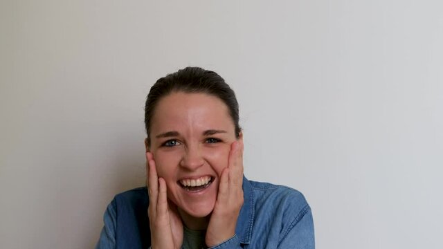 Young Caucasian European woman is pleasantly surprised and shocked and then starts laughing with huge beautiful smile. Girl in green Tshirt and denim shirt is emotional. 4K footage with emotions of pe