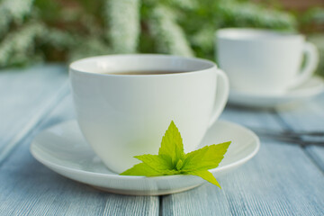 Two white porcelain cups with tea on a wooden table against a background of white flowers.