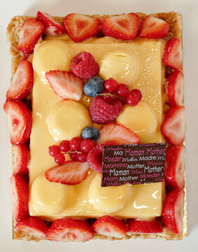 Mothers day fruit tart on plate, yellow cream with passion fruit flavor and red berries coulis on caramel crust, top view