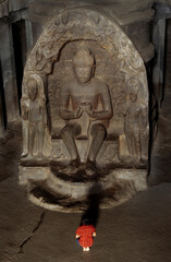 A girl in a red dress is sitting at the feet of the Buddha and praying. There is a very grand and linear statue of Buddha, Ellora caves, Aurangabad-India, UNESCO World Heritage Site