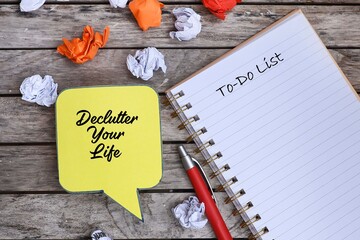 Bubble speech made from paper cutout with text on Declutter Your Life on the wooden plank.  A pen and notebook, and crumpled paper scattered around 