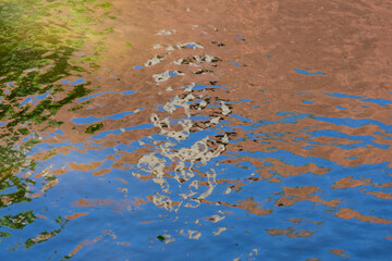 Abstract pattern in beige, brown and blue made by the reflection of a roof in the ripples of a water surface