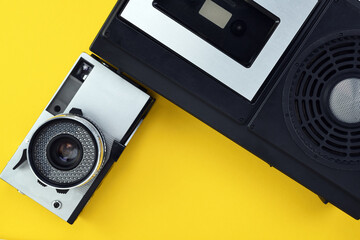 Old retro camera of the 1960s, 1970s in silver color and a cassette recorder on a yellow background.