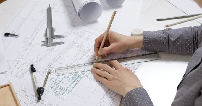 The hands of a professional architect draw a sketch of the design project with a pencil on paper. The desktop of a civil engineer creating blueprints for a building. 4K.