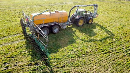 Traktor zieht Gülletonne und verteilt mittels Schleppschuhverteiler Gülle auf Wiese aus