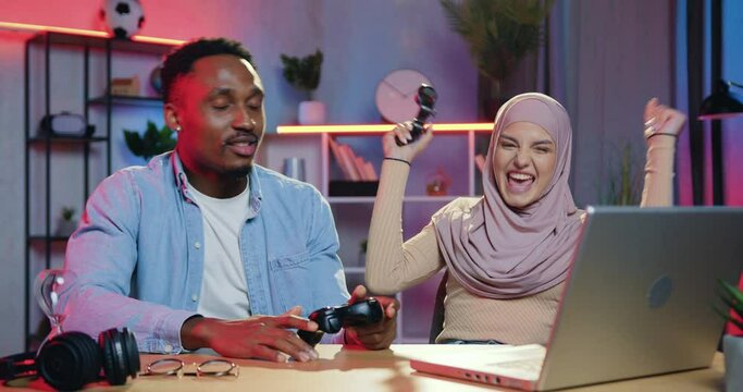 Human emotions concept where attractive positive modern young mixed races female and male friends having fun together at gaming on laptop,woman winning and deriding over mate-loser