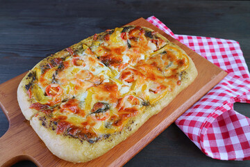 Mouthwatering fresh baked homemade pesto veggie pizza on a wooden breadboard