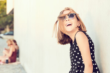 Portrait of a teenage argentinian girl wearing sunglasses and a polka dot dress, isolated over cement background. People in the background. Copy space.