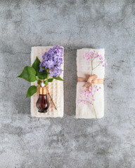 Vertical natural spa composition with white towels, bottle of serum and spring flowers on a grey textured background with copy space. Wellness, home skin care and spa relax treatment concept. Flat lay