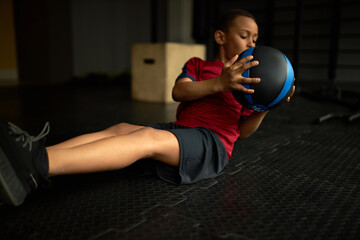 Active self determined little African boy wearing sports clothing and sneakers doing sit ups...
