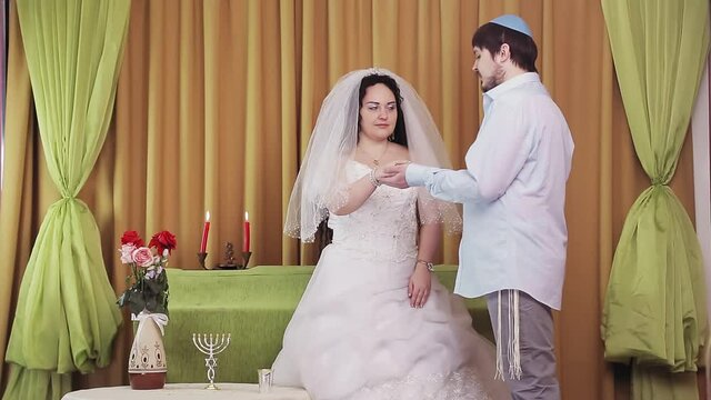 During the chuppah ceremony, a Jewish bride and groom in a synagogue puts a ring on the bride's index finger