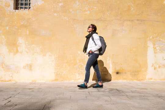 Tourist walking by the ancient medieval Mdina streets with a city backpack and enjoying a historical place. Smiling Female traveling alone on the Malta island.