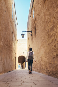 Female traveling alone on the Malta island. Tourist walking by the narrow ancient medieval Mdina streets with a city backpack and enjoying an historical place.