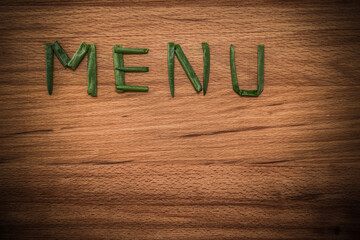 Onion petals folded in the form of the word 'MENU' on wooden table. Close-up view from above