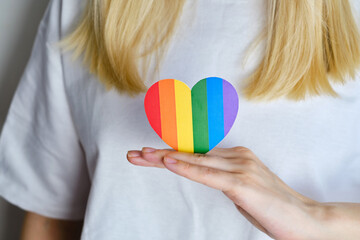 Rainbow heart from paper in woman hands in white t-shirt. LGBT flag. LGBTQIA Pride Month in June. Lesbian Gay Bisexual Transgender. Gender equality. Human rights and tolerance. Rainbow flag