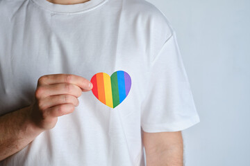 Rainbow heart from paper in man hands in white t-shirt. LGBT flag. LGBTQIA Pride Month in June....